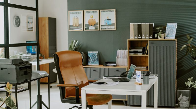 The 8 Leading Office Equipment Retailers Shaping the Global Supply Chain Modern office space with a brown leather chair, white desk, laptop, printer, and organized shelves with files and folders against a green wall.