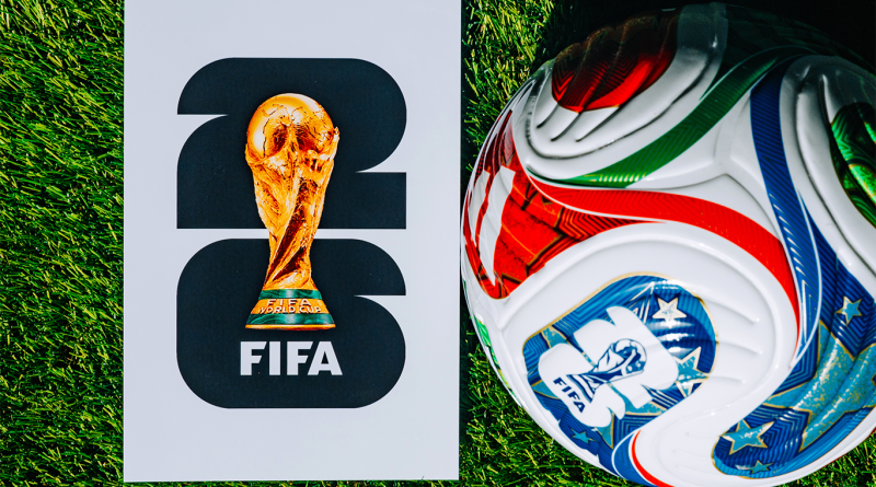 Official FIFA World Cup branding displayed on a white promotional panel featuring the World Cup trophy, positioned beside a football on green artificial turf.