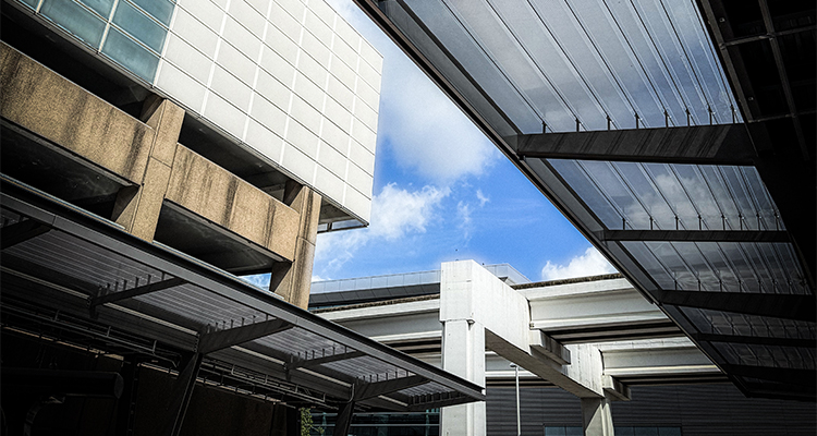 a low-angle architectural photograph of modern urban structures reaching toward a bright blue sky filled with scattered white clouds