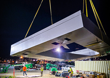 a massive central canopy section being lifted by a large crane at night