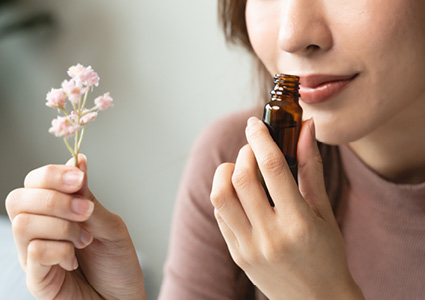 a person holding a sprig of baby's breath (Gypsophila) and smelling an amber glass dropper bottle
