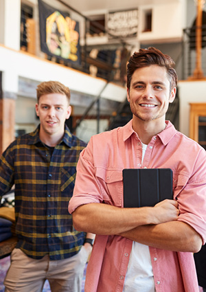 a smiling male fashion store owner or sales assistant holding a digital tablet with arms crossed